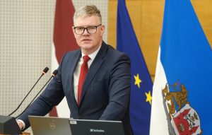 Rīgas domes priekšsēdētāja vietnieks Vilnis Ķirsis uzstājas ar runu pie tribīnes, fonā Latvijas un Eiropas Savienības karogi