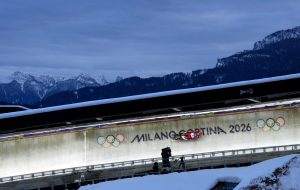 Kamaniņu braucēja Elīna Ieva Bota brauc pa ledus trasi ar uzrakstu “Milano Cortina 2026” kalnu ainavas fonā.