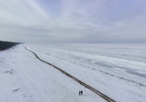 Aizsalusi jūras piekraste ziemā ar diviem cilvēkiem tālumā
