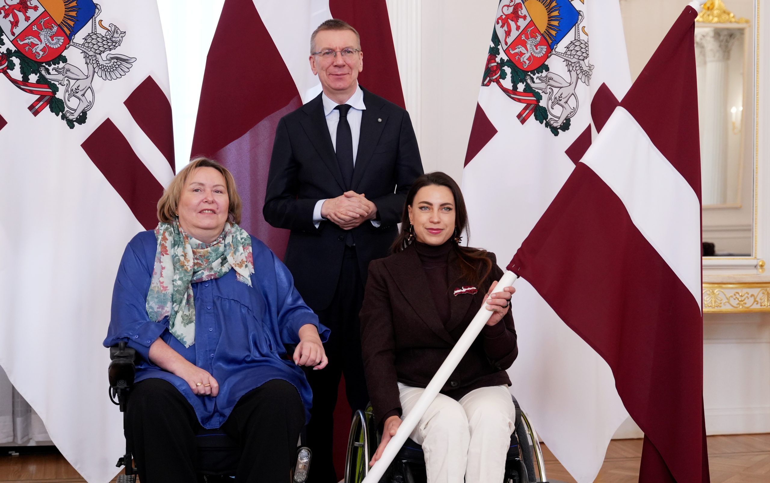 Valsts prezidents Edgars Rinkēvičs kopā ar divām parasportistēm pie Latvijas karogiem oficiālā tikšanās reizē.