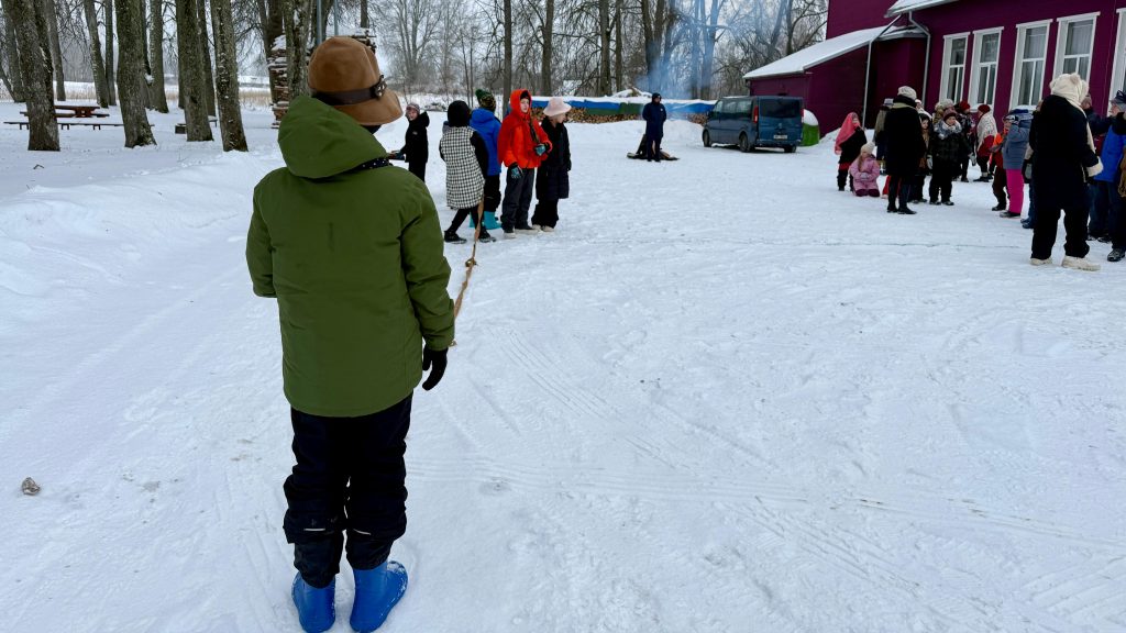 Bērns ziemas apģērbā stāv sniegotā laukumā un tur virvi Meteņdienas aktivitātēs Leimaņos