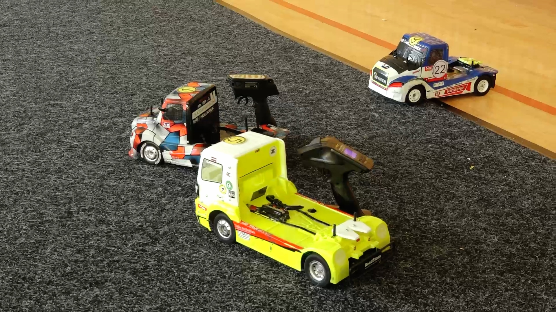 Radiovadāmie automodeļi un pultis uz paklāja trases iekštelpās sacensību laikā.