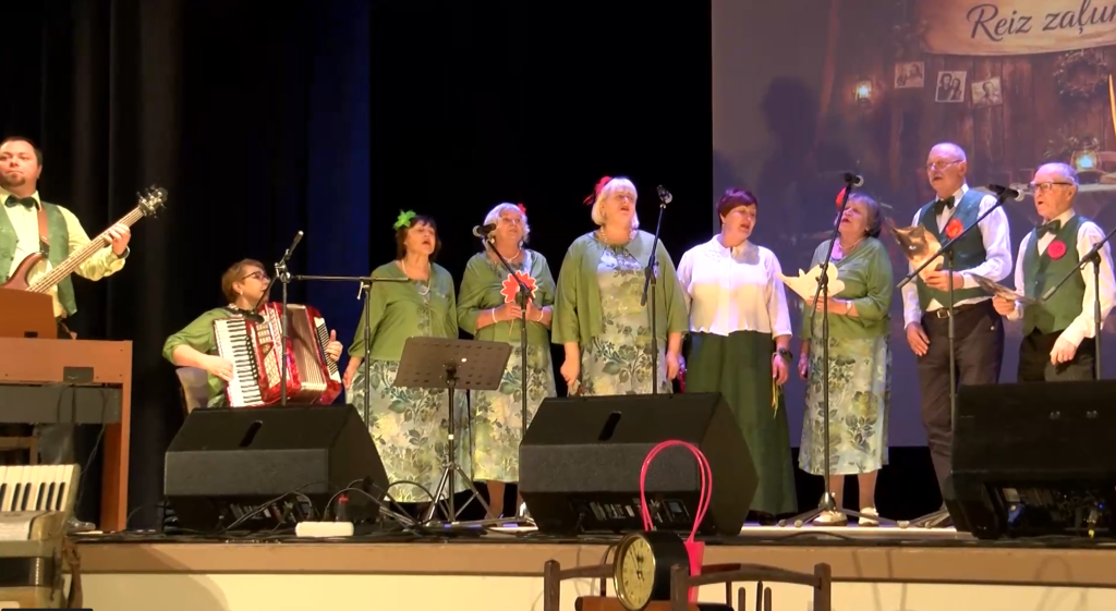 Senioru ansamblis uz skatuves ar akordeonistu koncertā