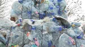 Saspiestu plastmasas pudeļu kaudze ar zilām korķu vāciņu malām, pārklāta ar sniegu ziemas apstākļos.
