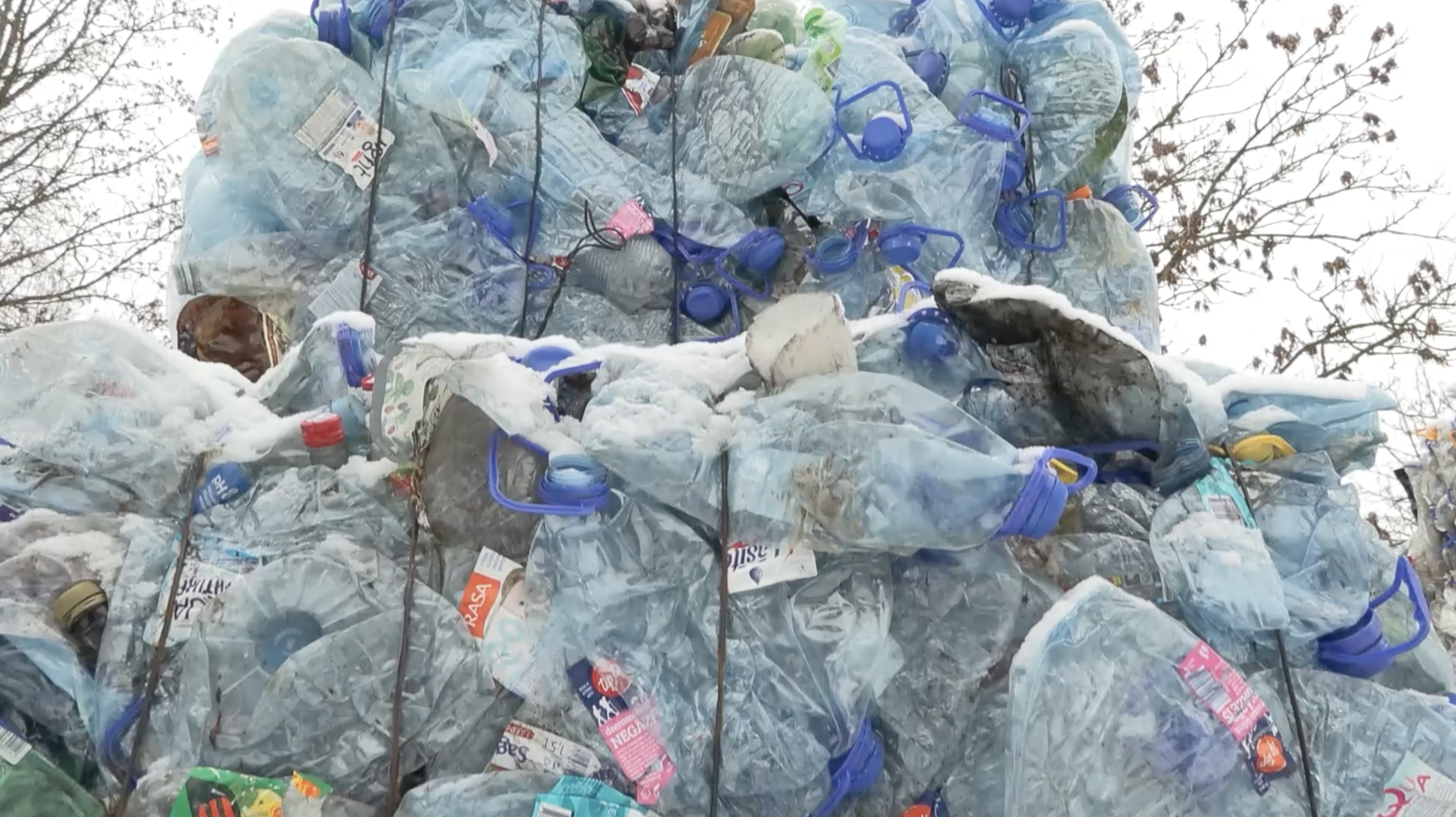 Saspiestu plastmasas pudeļu kaudze ar zilām korķu vāciņu malām, pārklāta ar sniegu ziemas apstākļos.