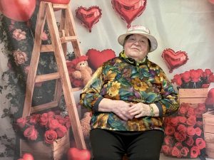 83 gadus vecā Veronika pozē portreta foto ar sirsnīgu smaidu, fonā sirds un ziedu dekori.