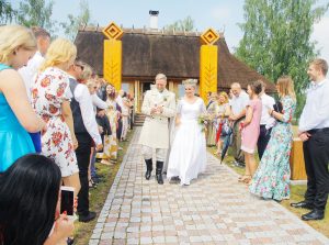 Jaunlaulātie iznāk no lauku mājas, viesiem stāvot abās pusēs un sveicot pāri ar ziediem.