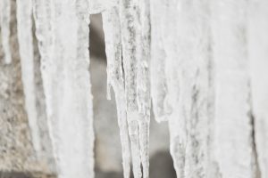 Tuvplānā redzamas garas lāstekas pie sniegotas jumta malas ziemā