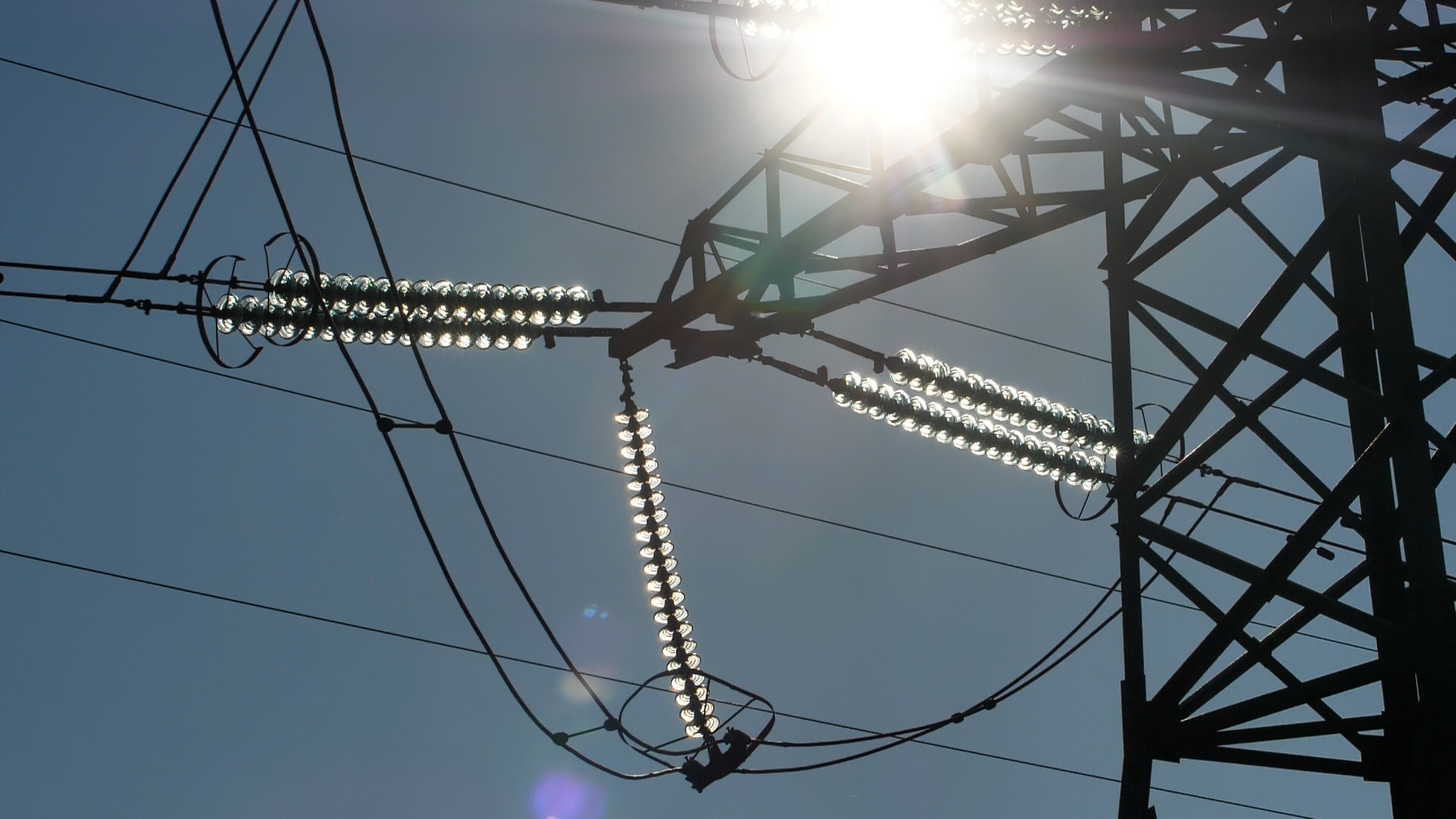 Elektropārvades līniju konstrukcijas un vadi spožā pusdienlaika saulē.