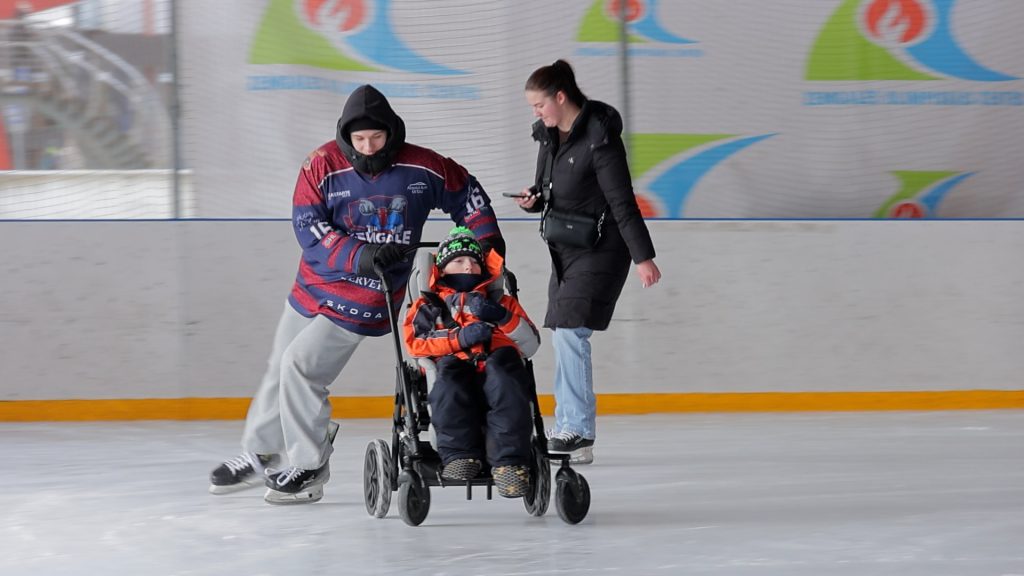 Jaunietis stumj bērnu ratiņkrēslā pa ledu Jelgavas slidotavā