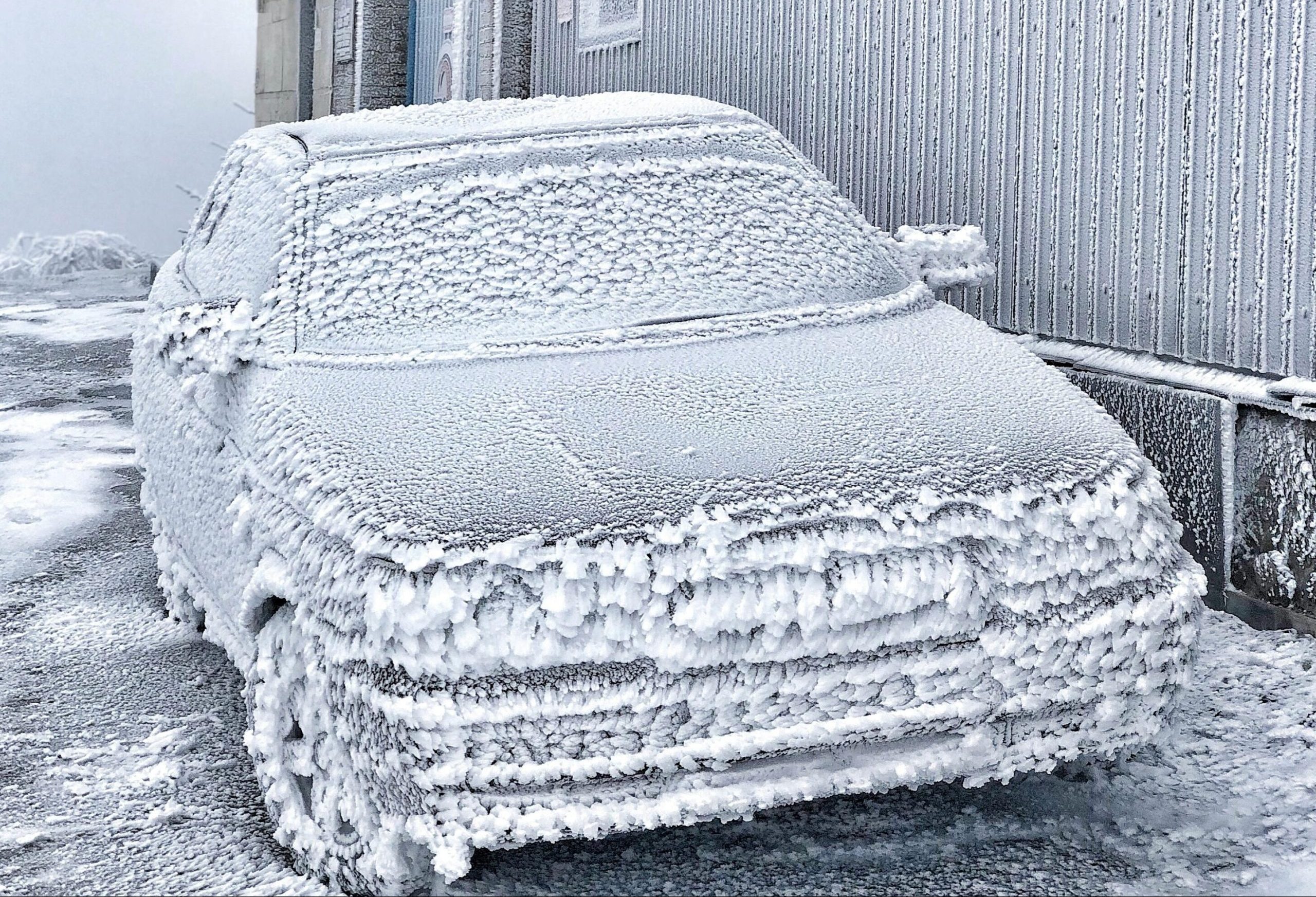 Ar biezu sarmu klāts vieglais automobilis pie ēkas stiprā salā