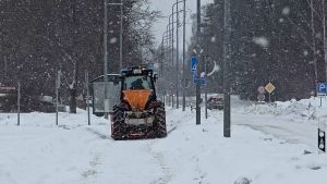 Traktors kaisa pretslīdes materiālu uz sniegotas pilsētas ielas intensīvas snigšanas laikā.