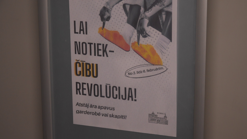 Akcijas "Lai notiek čību revolūcija!" plakāts pie sienas ar aicinājumu atstāt āra apavus garderobē.