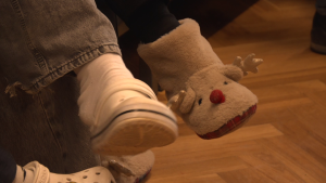 Tuvplāns ar bērnu kājām, kuram vienā kājā ir gaiša "Crocs" tipa čība, bet otrā — pūkaina ziemeļbrieža čība.