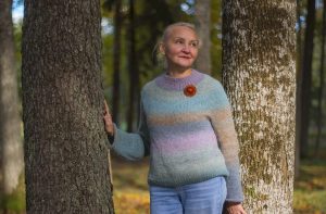 Iveta Skudra stāv mežā starp kokiem un raugās sānis dabas vidē.