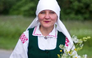 Iveta Skudra latviešu tautastērpā ar pļavas ziediem rokās.