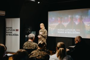 Nacionālo bruņoto spēku pārstāve uzstājas auditorijas priekšā prezentācijā par kampaņu “Mana Latvija – mana atbildība”.