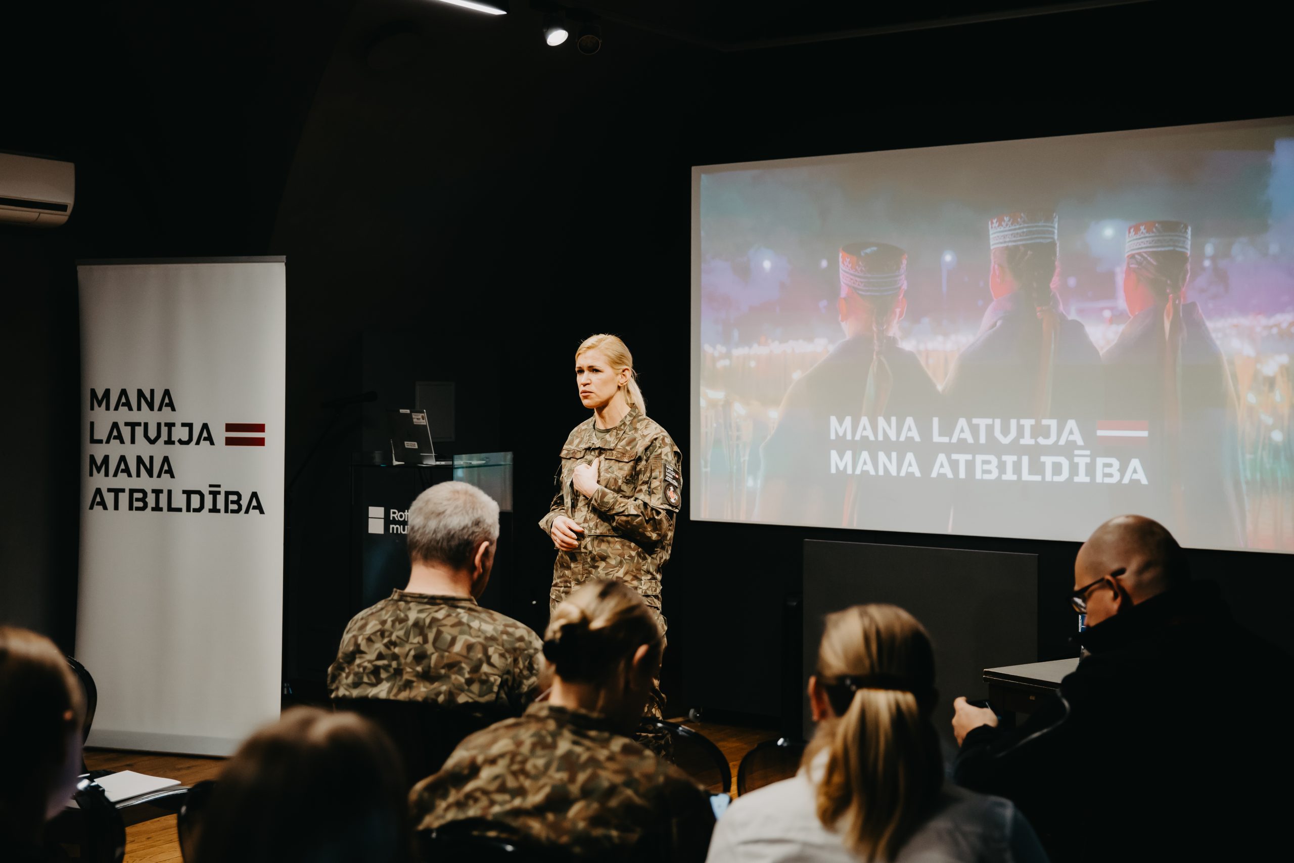 Nacionālo bruņoto spēku pārstāve uzstājas auditorijas priekšā prezentācijā par kampaņu “Mana Latvija – mana atbildība”.