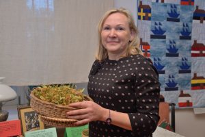 Sieviete tur rokās grozu ar kaltētiem liepziediem izstādē.