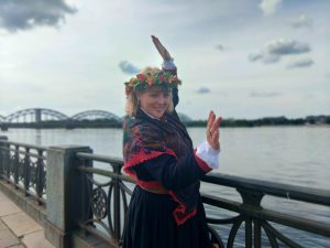 Sieviete tautastērpā ar ziedu vainagu pie Daugavas.