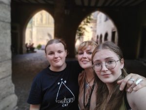Folkloras grupas dalībniece ar meitām vēsturiskā pilsētas pagalmā.