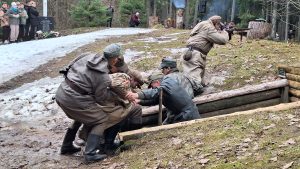 Vēsturiskās kaujas rekonstrukcijā karavīri palīdz ievainotajam pie partizānu bunkura.
