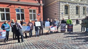Cilvēku grupa ar plakātiem piedalās protestā pret vēja parkiem pilsētā.