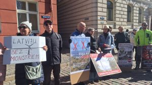 Cilvēki ar plakātiem piedalās protestā pret vēja parkiem pilsētvidē.