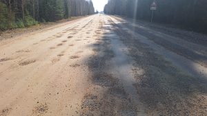 Bedrains grants ceļš meža vidū ar redzamiem bojājumiem