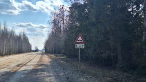 Ceļa zīme brīdina par nelīdzenu grants ceļu meža teritorijā