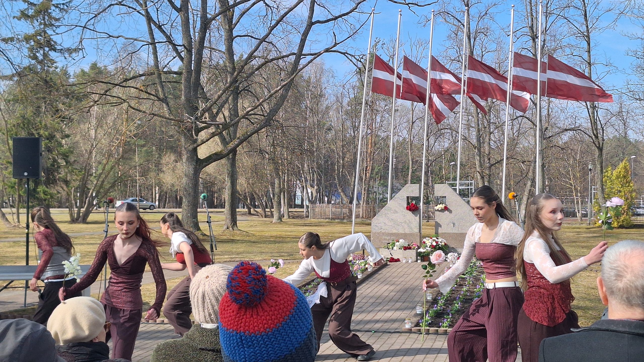 Jaunieši dejas performancē piemin deportāciju upurus pie pieminekļa ar Latvijas karogiem.
