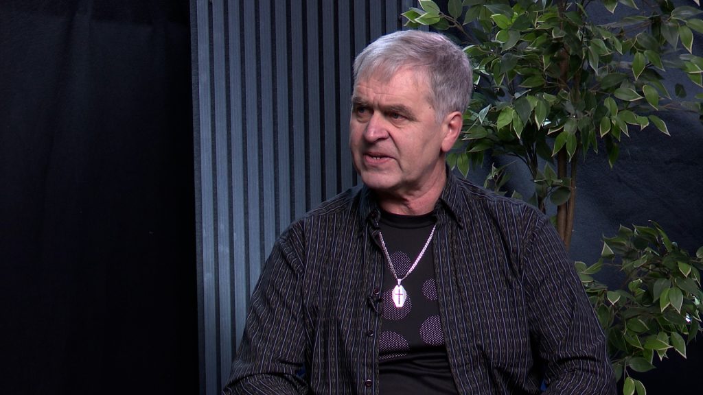 Aivars Lapšāns tumšā kreklā sēž studijā un runā sarunas laikā