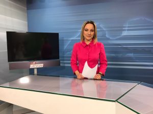 Ziņu diktore studijā pie galda ar lapu rokās