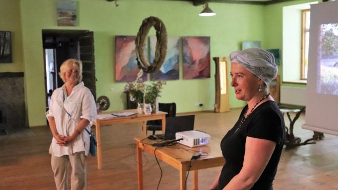Daina Alužāne runā pasākumā mākslas telpā pie projektora
