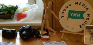 Fotoaparāti un “Young Media House” logo Dzērbenes jauniešu digitālā satura nometnē.