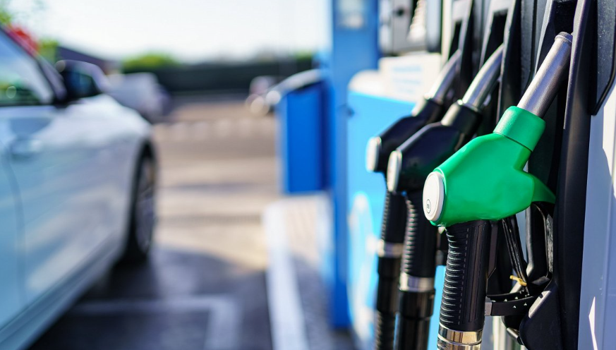 Degvielas uzpildes pistoles degvielas stacijā ar automašīnu fonā.