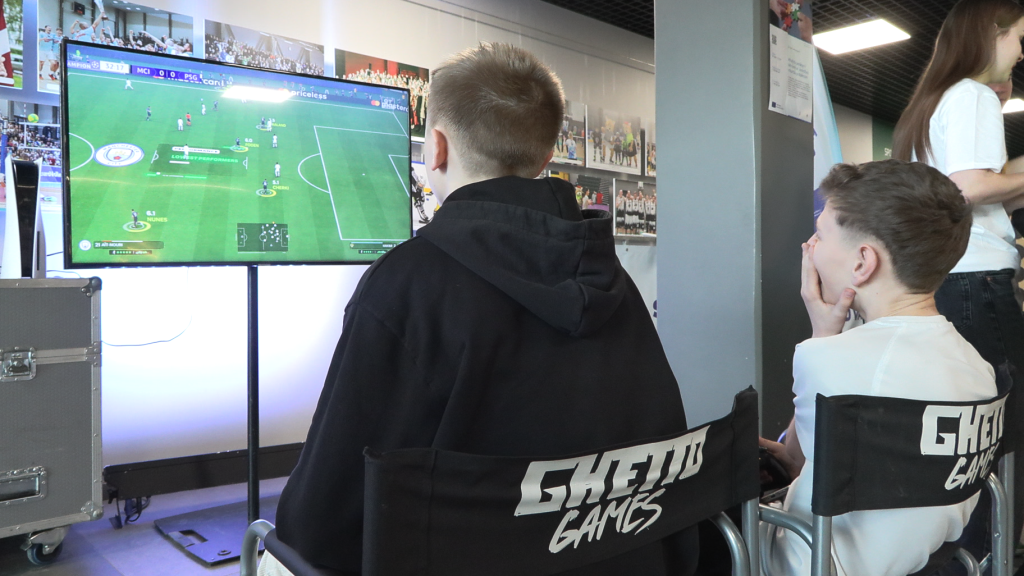 Jaunieši spēlē futbola videospēli uz lielā ekrāna