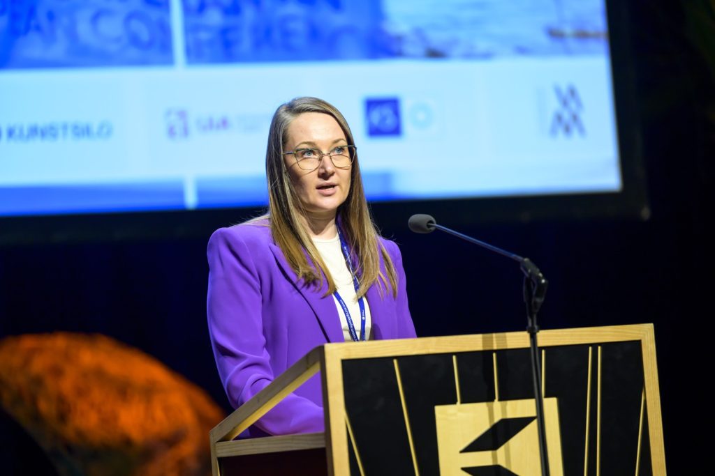 Guna Puce uzstājas pie tribīnes konferencē