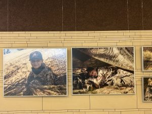 Fotogrāfiju izstādē redzami attēli ar jauniem karavīriem militārajās mācībās dabā.