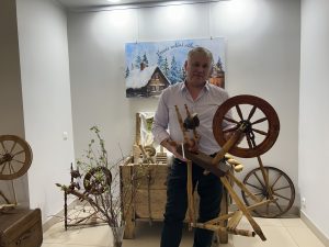 Vīrietis tur vērpjamo ratiņu muzeja ekspozīcijā