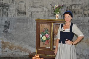 Ilona Kangizere tradicionālā tērpā pie muzeja ekspozīcijas.