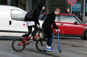 Jaunieši pārvietojas ar velosipēdu un elektroskrejriteni pilsētā.