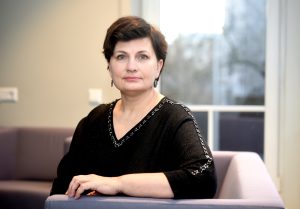 Ilze Viņķele sēž krēslā iekštelpās, portreta foto ar neitrālu fonu.
