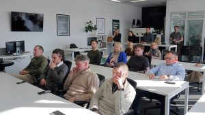 Cilvēki klausās prezentāciju seminārā biroja telpās