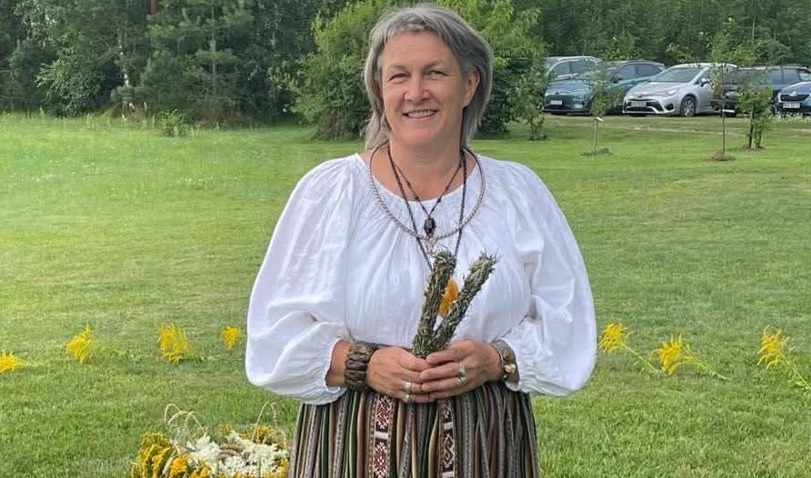 Olita Puriņa tautiskā apģērbā ar zāļu saišķi rokās