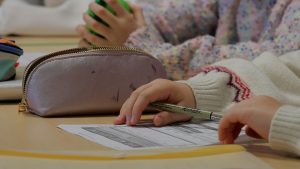 Skolēns klasē pilda uzdevumu uz lapas ar pildspalvu