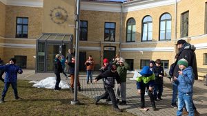 Bērni ārā pie skolas met papīra lidmašīnas pagalmā.