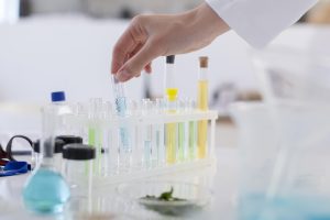 Laboratorijā pētnieks tur mēģeni ar šķidrumu starp citām mēģenēm.