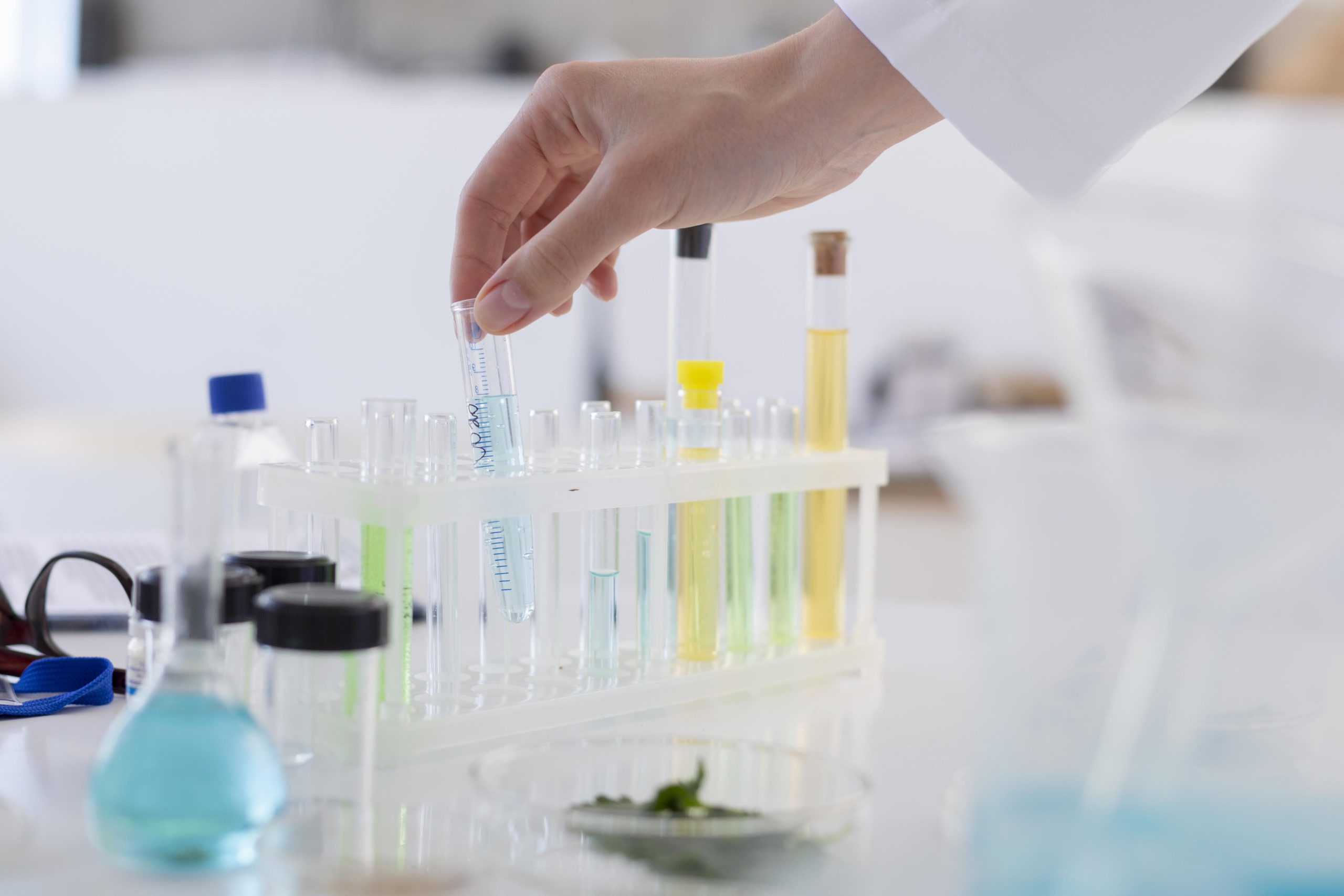 Laboratorijā pētnieks tur mēģeni ar šķidrumu starp citām mēģenēm.