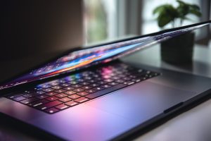 Klēpjdators ar apgaismotu tastatūru un daļēji aizvērtu ekrānu